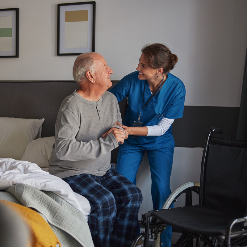 nurse helping patient out of bed and into a wheelchair