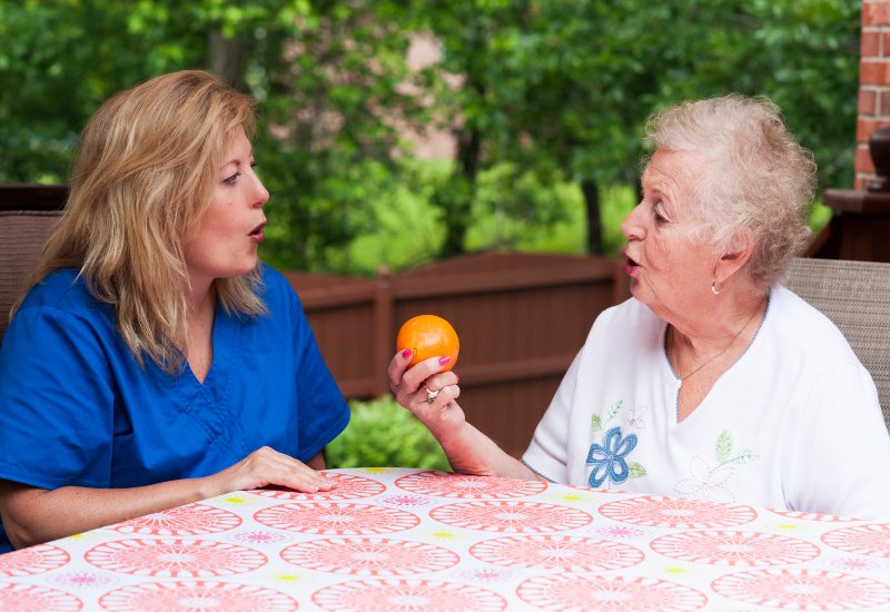 An older adult and caregiver talking during speech therapy while holding an orange in Glenview, IL