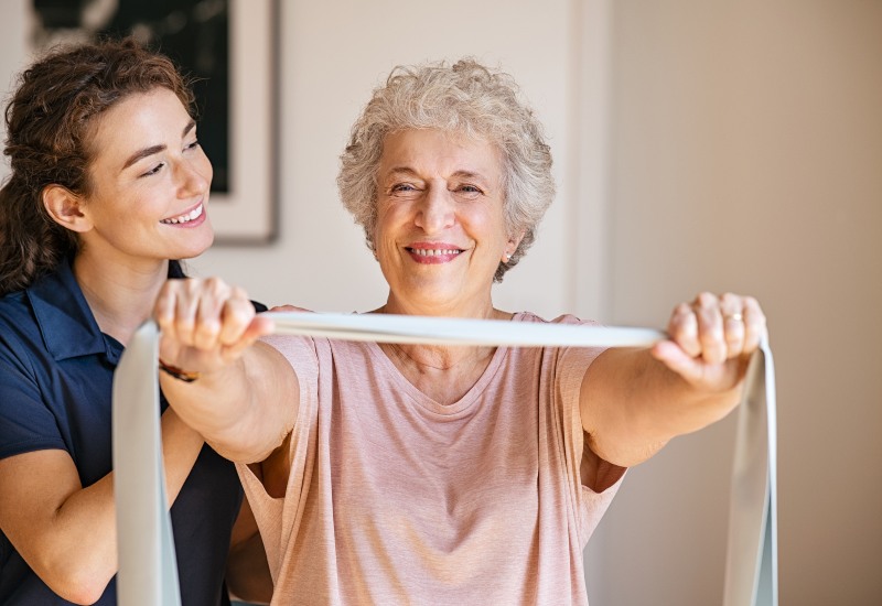 Senior doing resistance band exercise with caregiver support in Glenview & Northbrook, IL