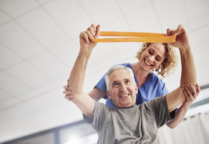 A senior doing resistance band exercise with a therapist assistance in Glenview, IL